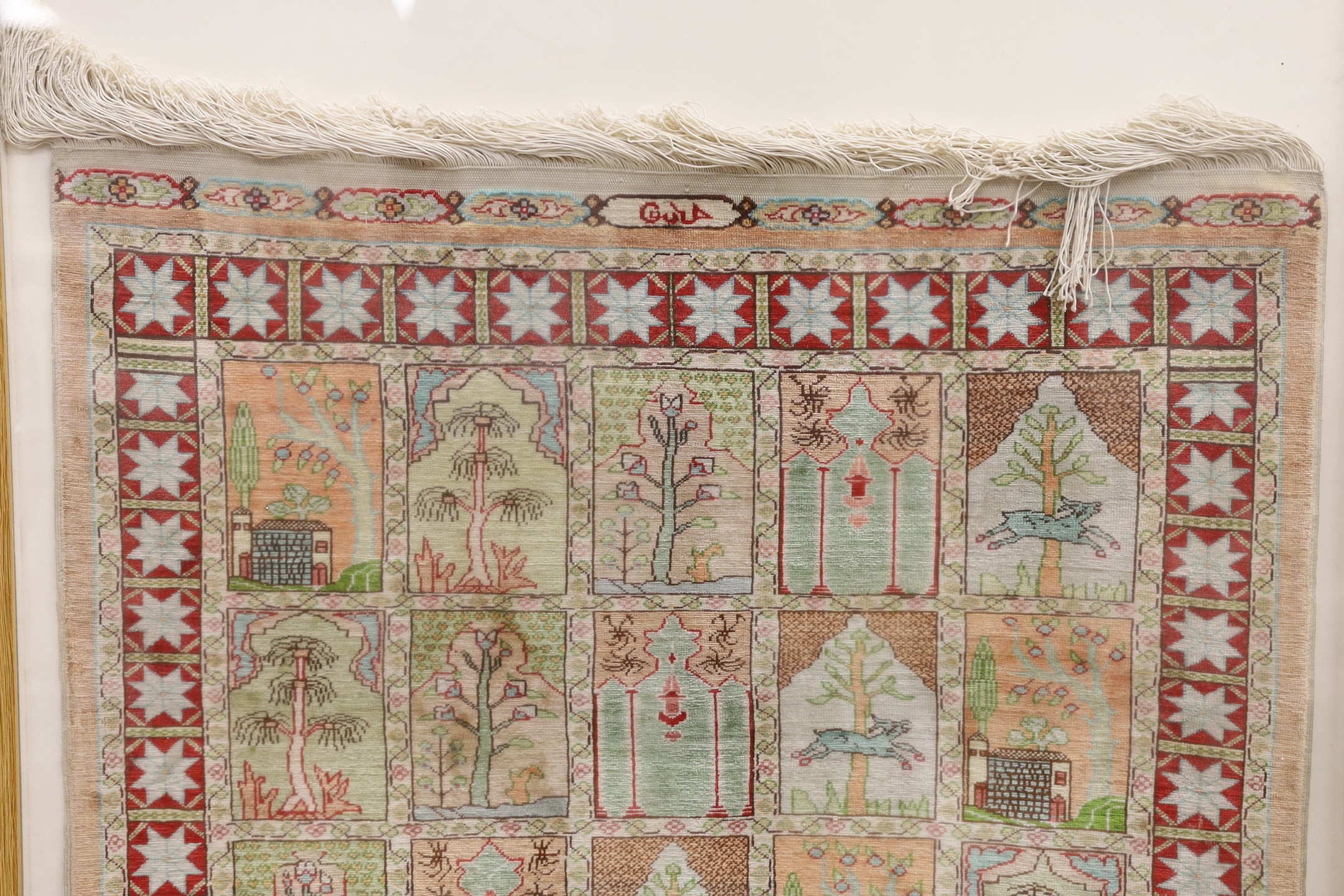 An Eastern framed silk rug depicting trees amimals and buildings, 86 cms high x 67cms wide